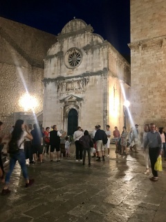A floodlit church and the evening crowd drifting past it.