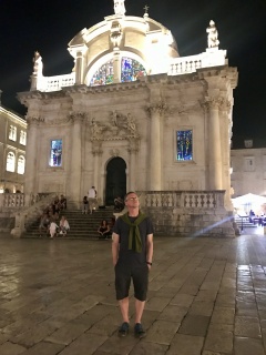 Brian and a baroque facade, both lit up and posing.