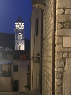 Bell tower lit white down the alley after dark.