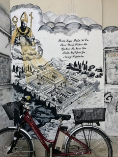 Dinner at the Uje Oil Bar. A painted map of the Palace, a saint, and a red bike parked to scale.